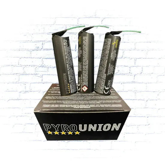 Drei schwarze zylindrische Feuerwerkskörper mit Zündschnur aus dem Pyrounion P1 6er Pack von Pyrounion stehen aufrecht auf einer schwarzen "PYRO UNION"-Schachtel mit gelben Sternen vor einem weißen Backsteinmauer-Hintergrund.